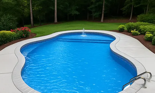 Luxurious curved backyard pool with blue water and white deck surrounding lush landscaping