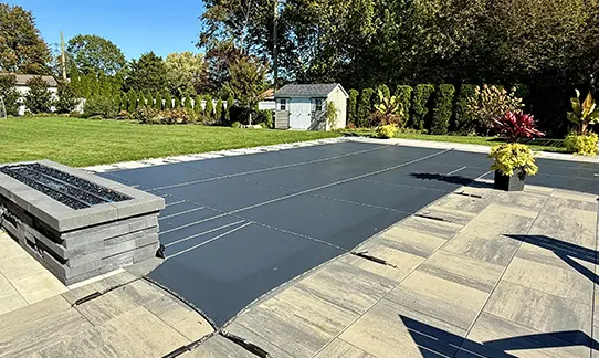 Modern backyard pool with dark cover surrounded by patio and landscaping