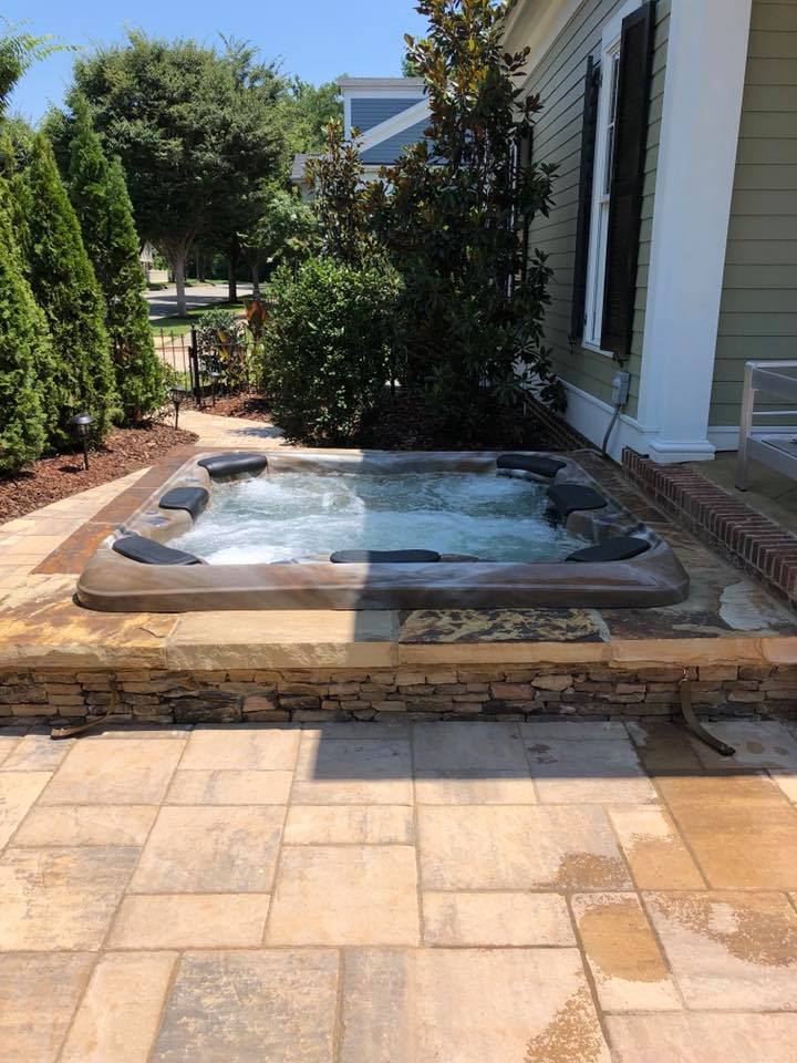Modern backyard spa installed on stone patio beside residential home