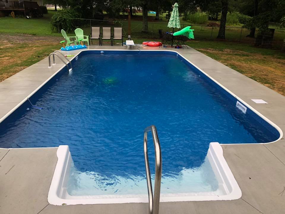 Rectangular backyard pool with concrete deck and metal ladder for residential swimming