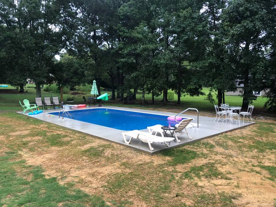 Backyard pool with white decking surrounded by lounge chairs and tall trees
