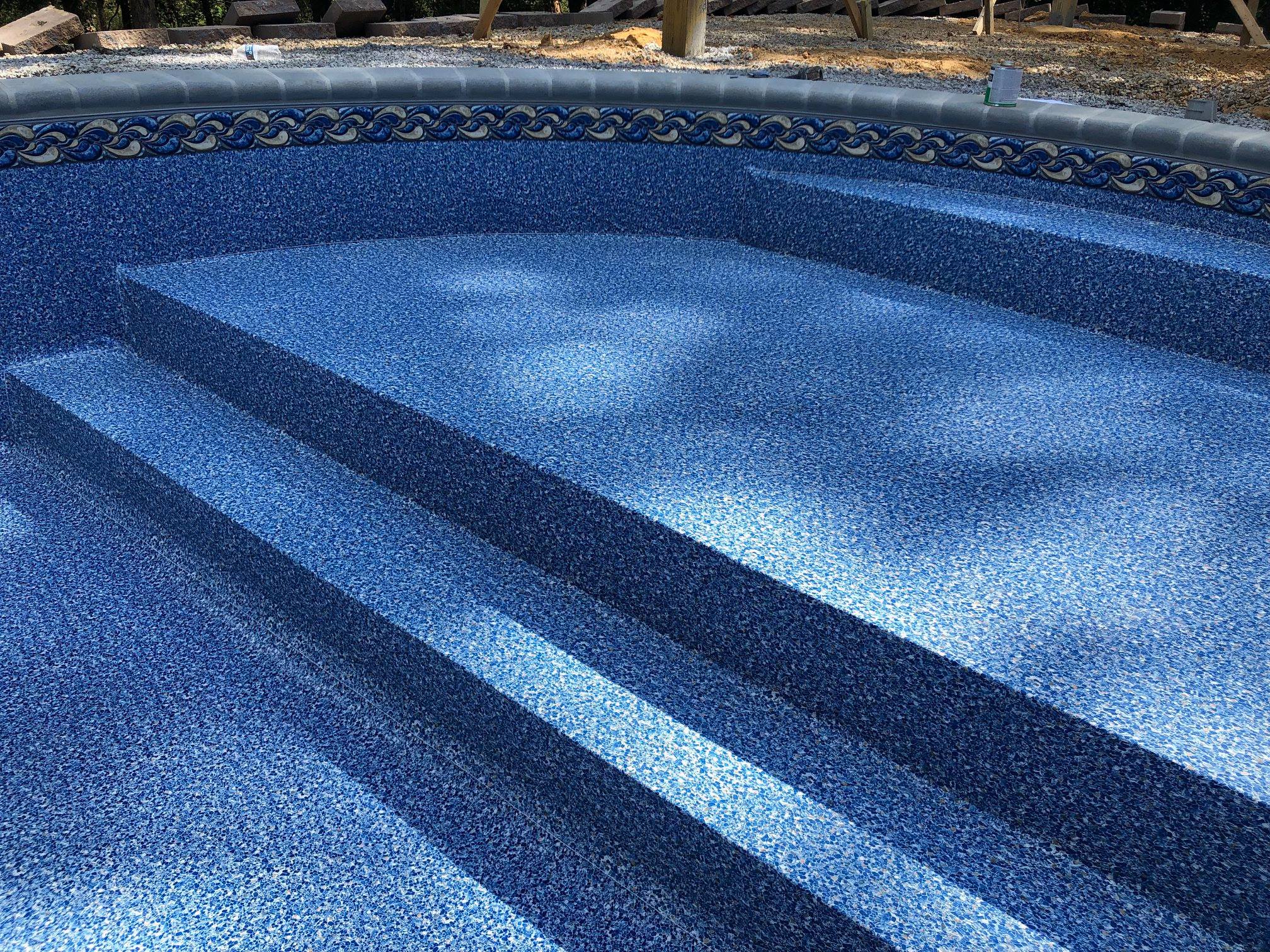 Empty residential backyard pool with blue mosaic tile interior and decorative border