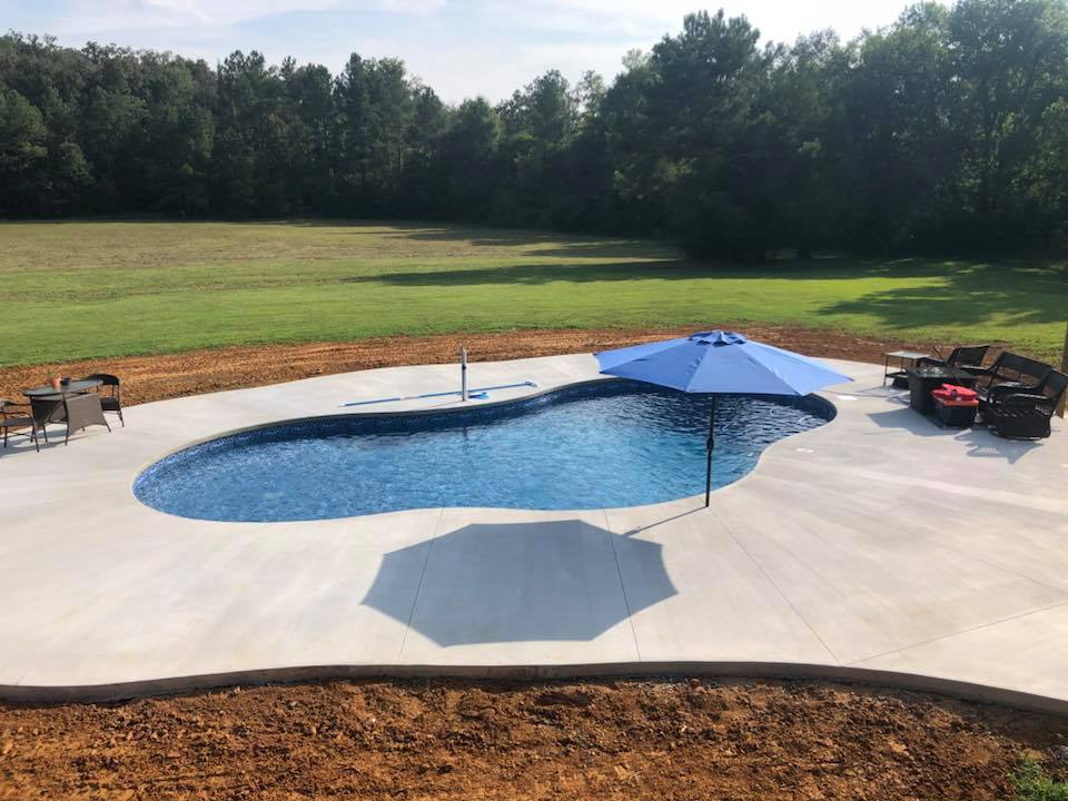 Modern backyard pool with concrete deck, blue umbrella, and surrounding landscape for residential spa ownership