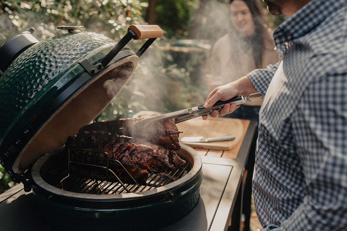 Man grilling meat on green egg-style outdoor smoker in backyard