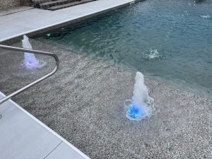 Modern backyard pool with illuminated water jets and spa features at dusk