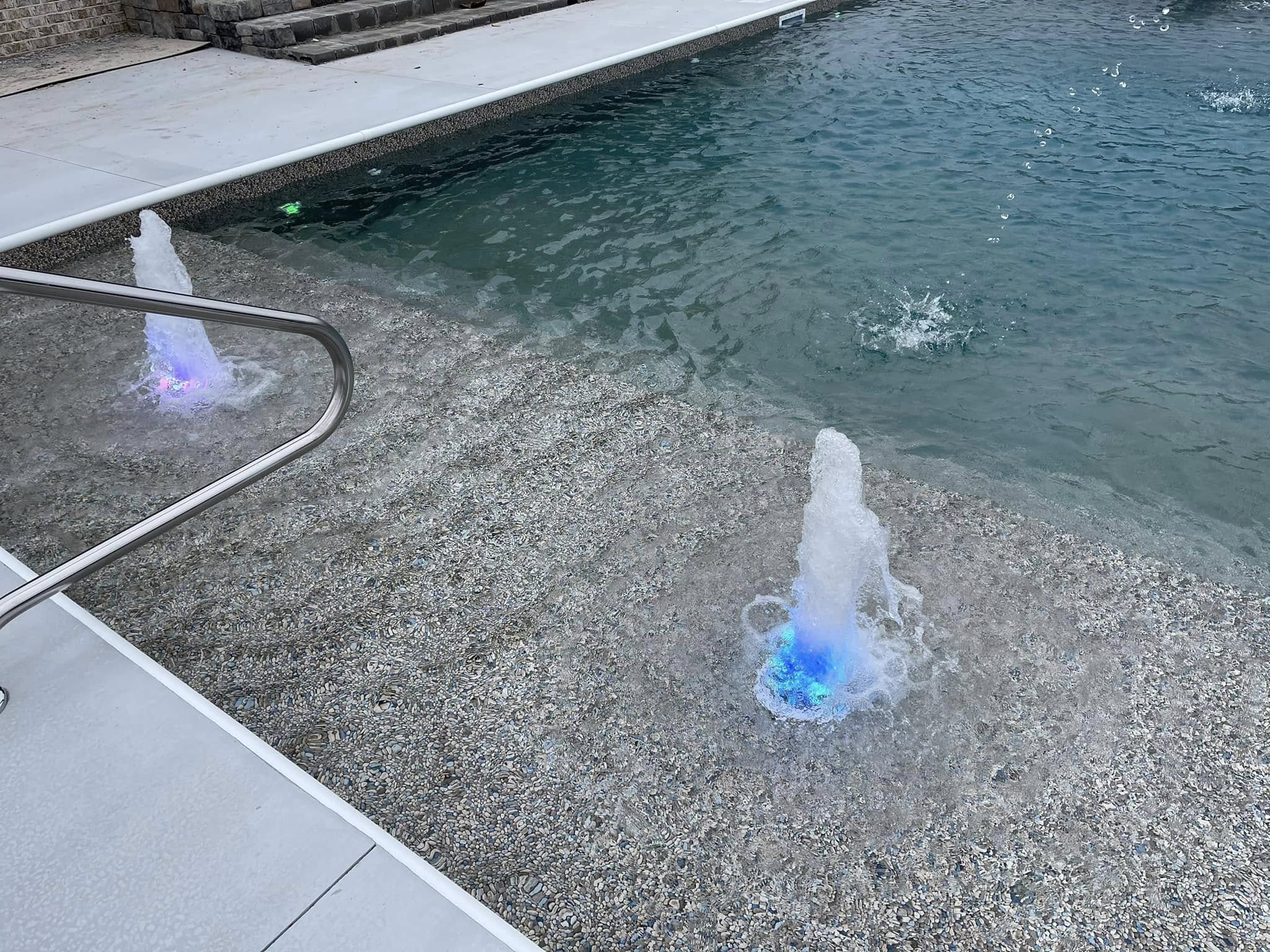 Modern backyard pool with illuminated water jets and spa features at dusk