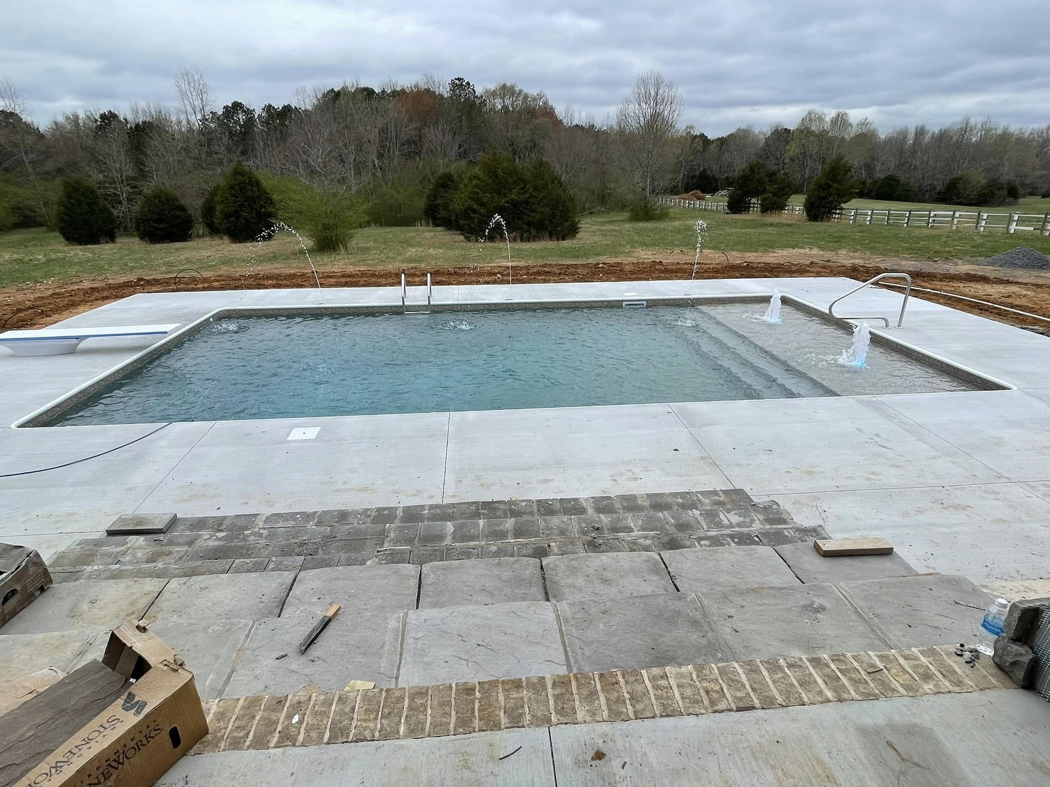 Newly installed residential backyard pool with concrete decking and surrounding landscape during construction