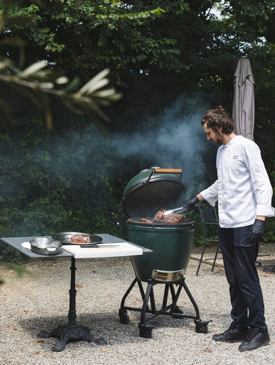 Man cooking meat on green ceramic outdoor grill in backyard setting
