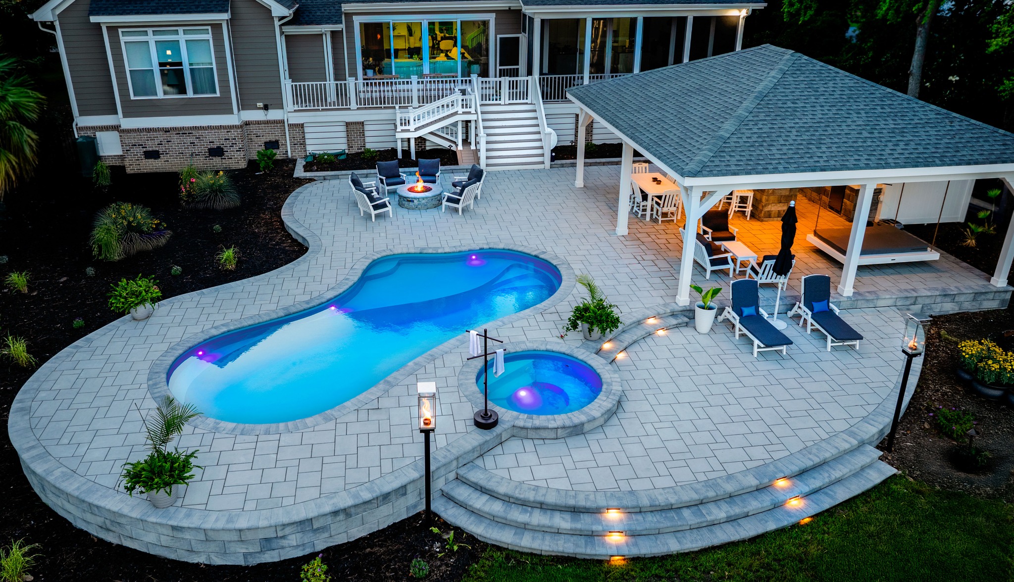 Luxurious backyard residential spa and pool setup with illuminated hot tubs at night