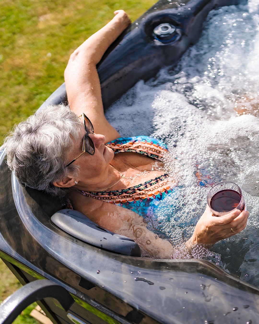 Senior woman relaxing in inflatable hot tub with drink outdoors