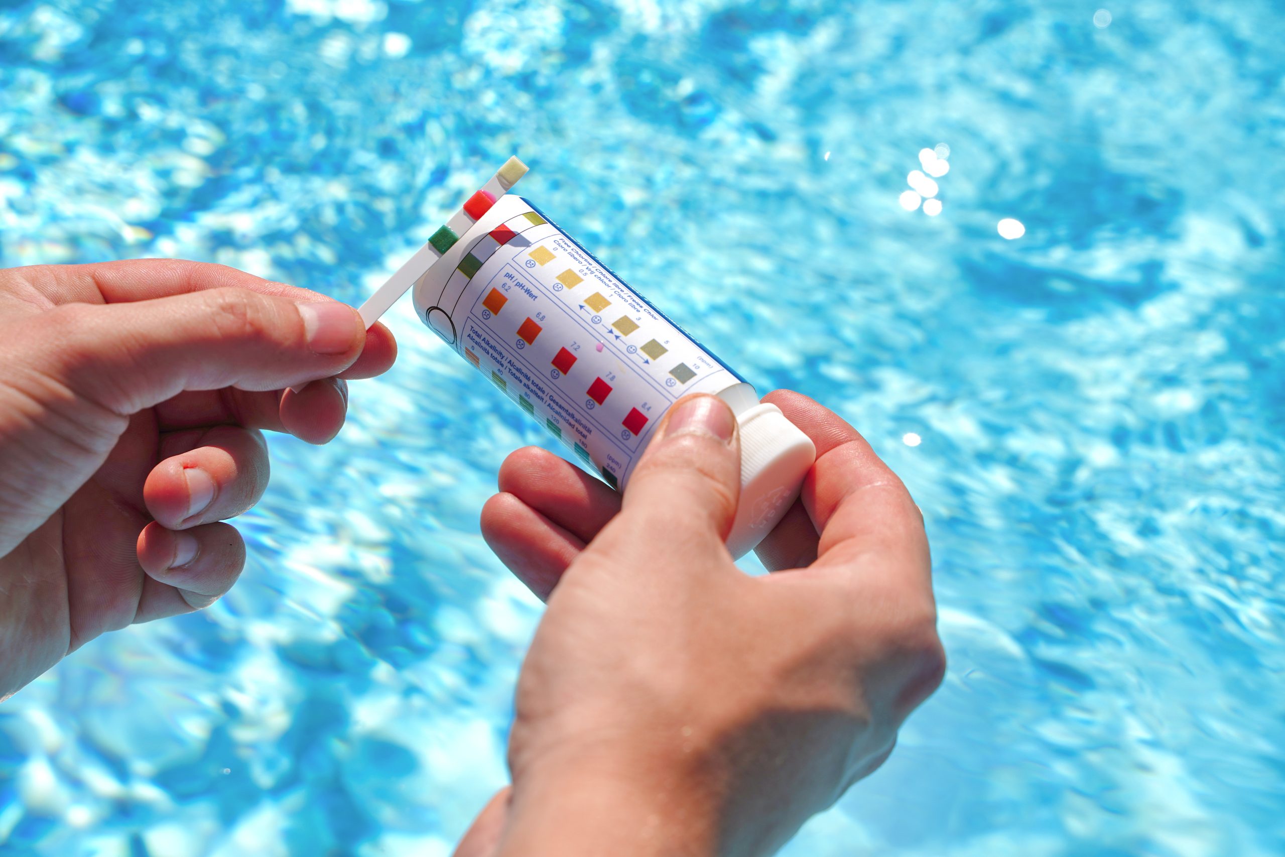 Person holding pool water testing kit for hot tub maintenance and backyard pool care