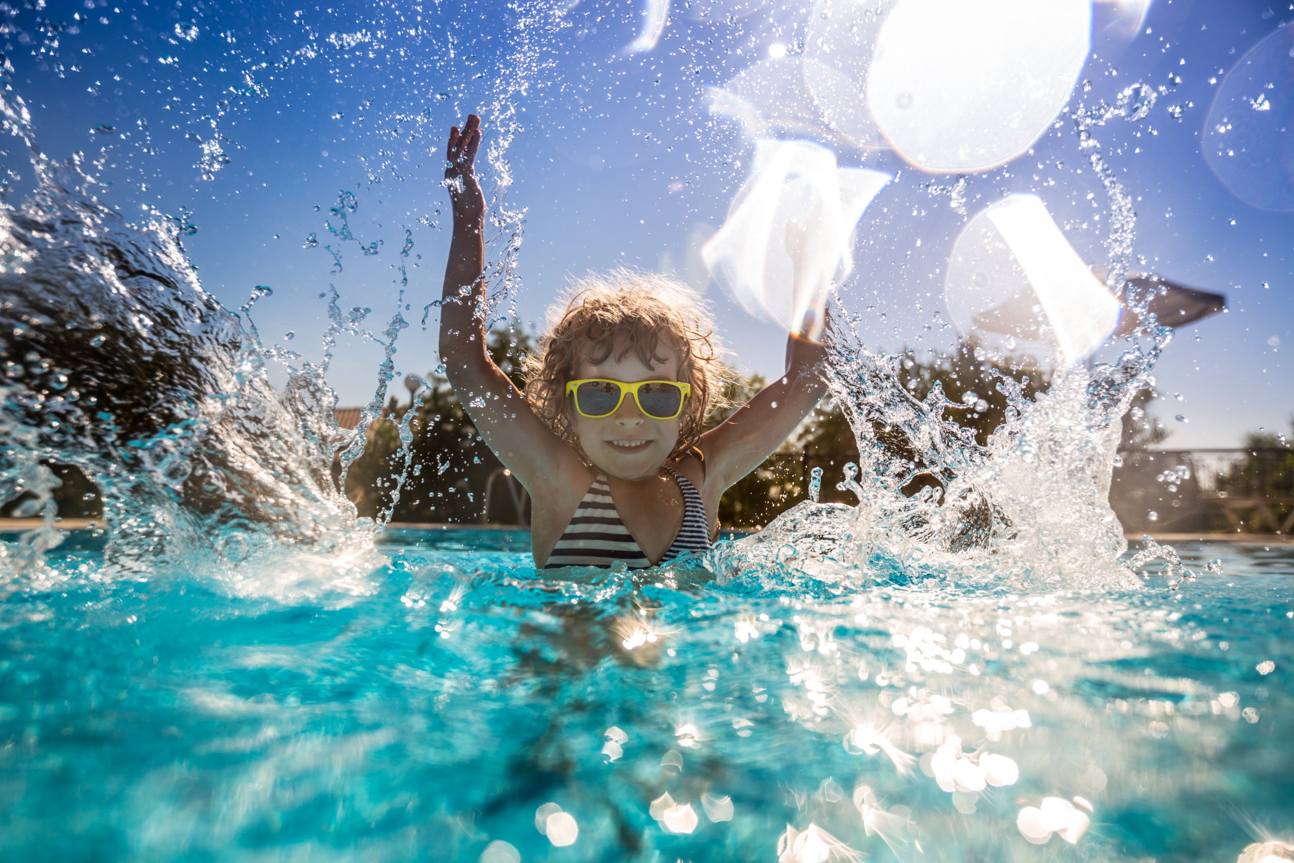 Happy child splashing in a bright blue backyard pool on a sunny day