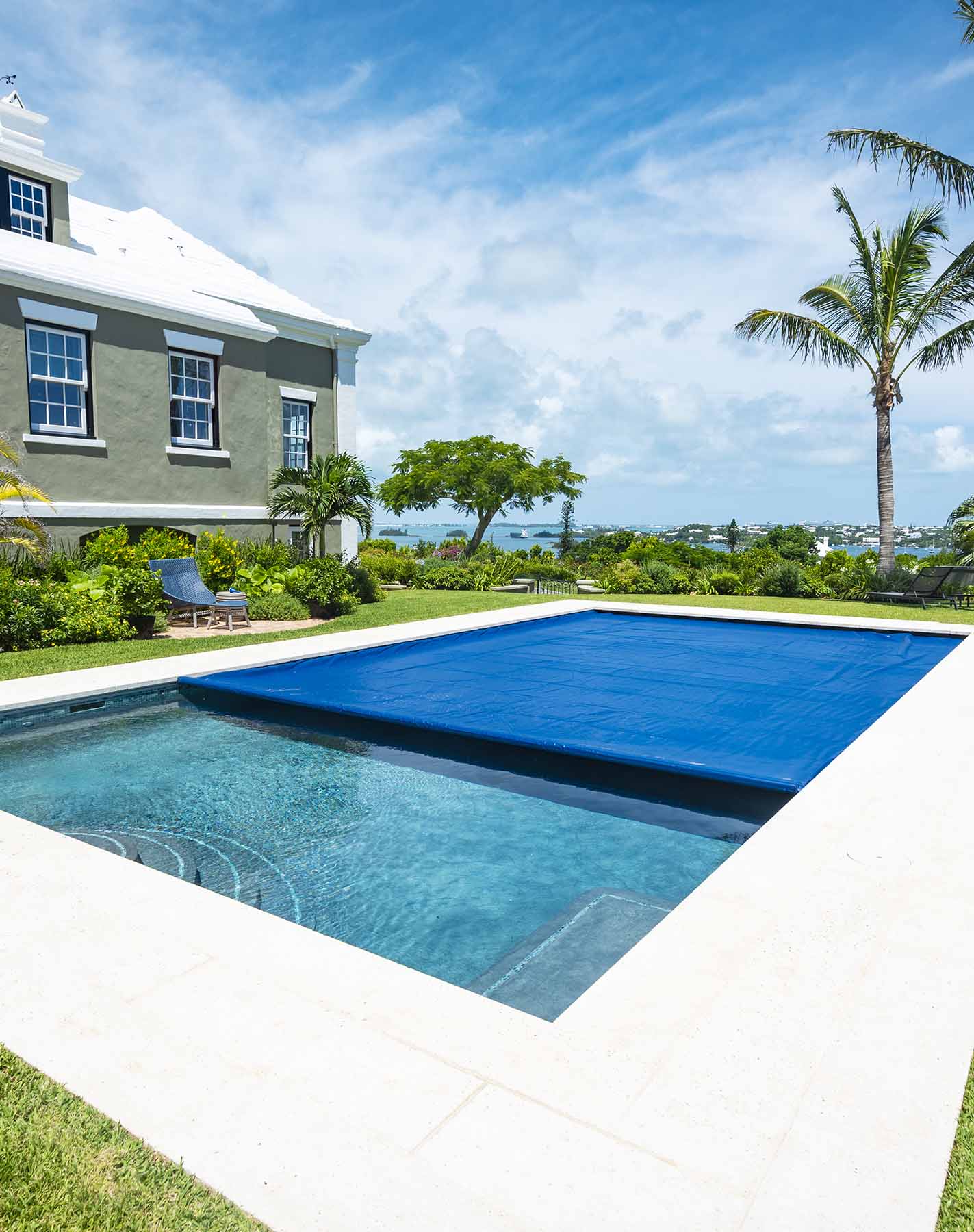 Luxury backyard pool with blue cover next to elegant residential home and manicured landscaping