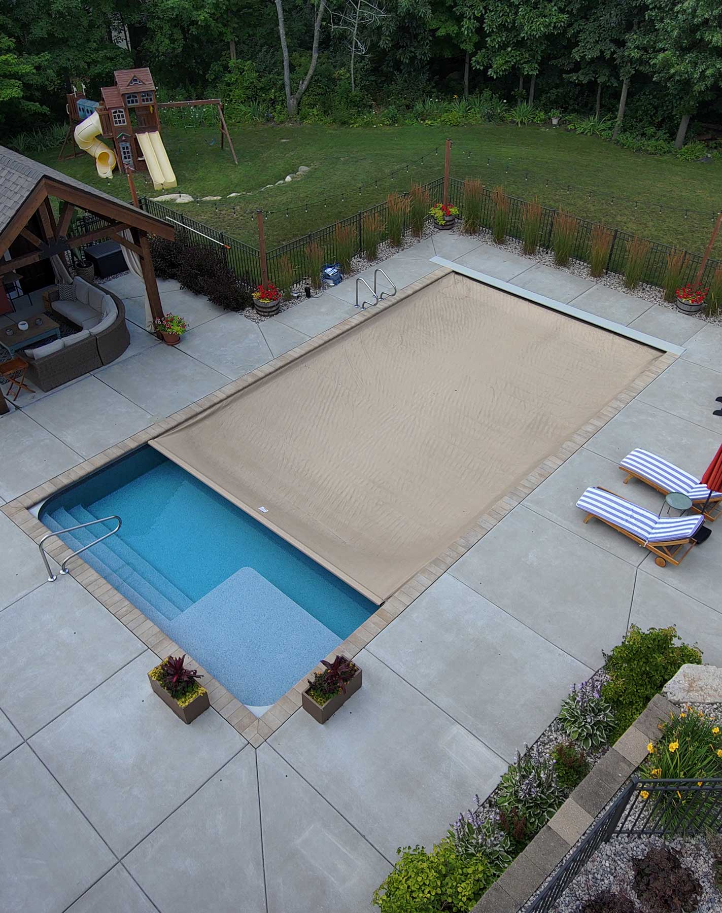 Covered residential swimming pool with lounging chairs and manicured backyard patio
