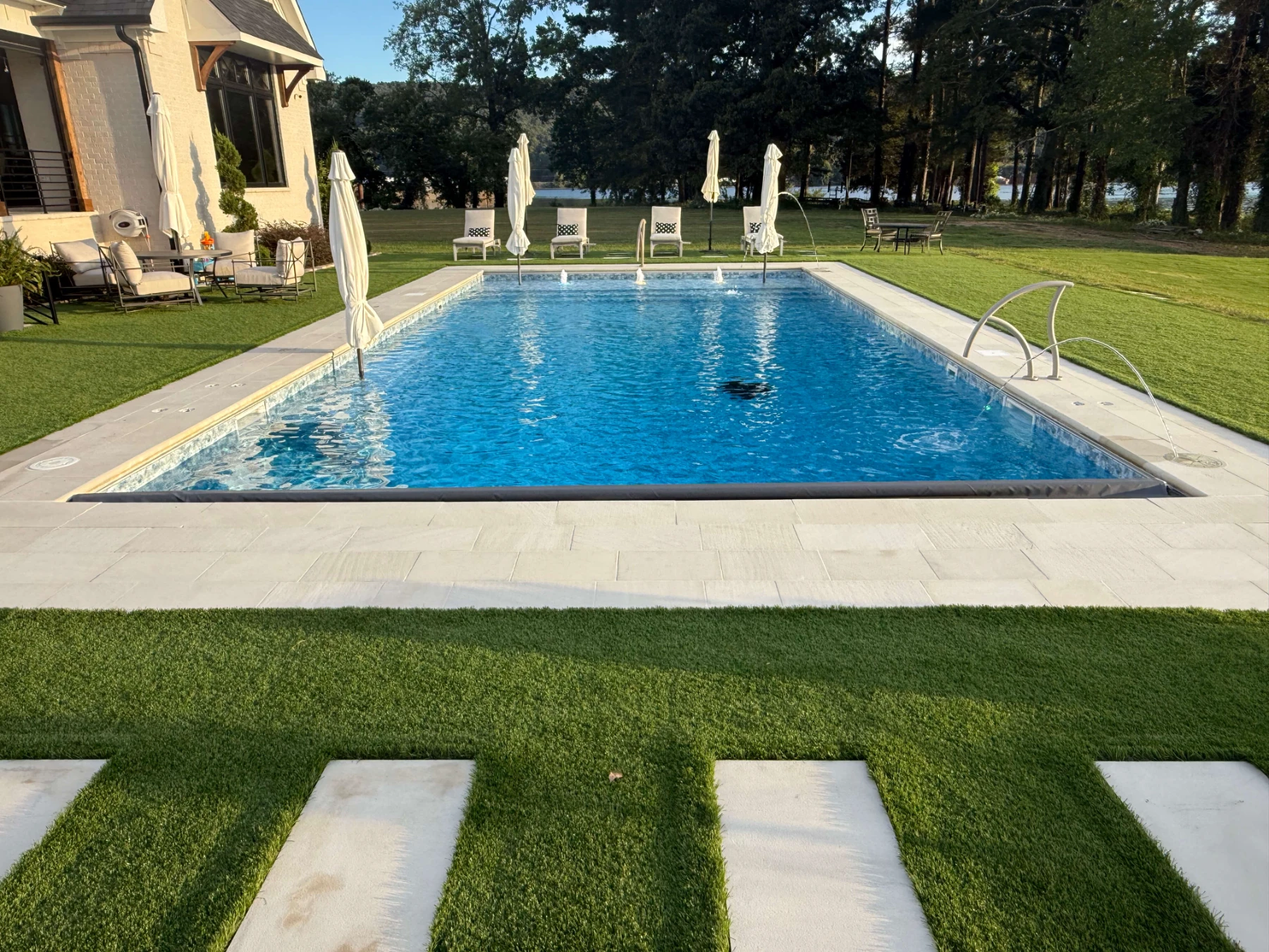 Luxury backyard pool with lounge chairs, umbrellas, and manicured lawn surrounding resort-style residential spa