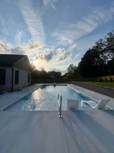 Modern backyard pool with lounge chairs and pool house at sunset