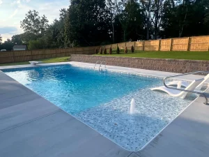 Modern backyard pool with shallow entry area and wooden privacy fence